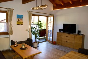 Sala de estar com mesa de jantar de madeira, sofá, televisão e planta em vaso.