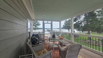 A covered porch with wicker furniture, a small table, and a view of a lake.