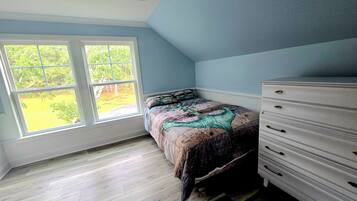 A bedroom with a bed, dresser, and large windows.