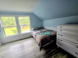Ein Schlafzimmer mit Bett, Kommode und großen Fenstern.