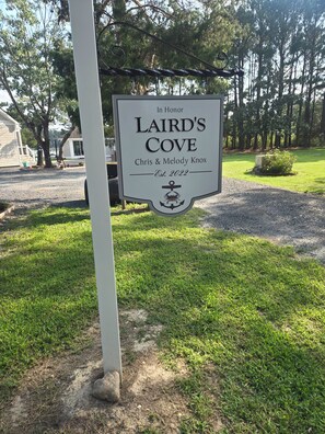 Skilt for 'Laird's Cove', opstillet i 2022, til ære for Chris & Melody Knox, med et baggrund af træer og en grussti.