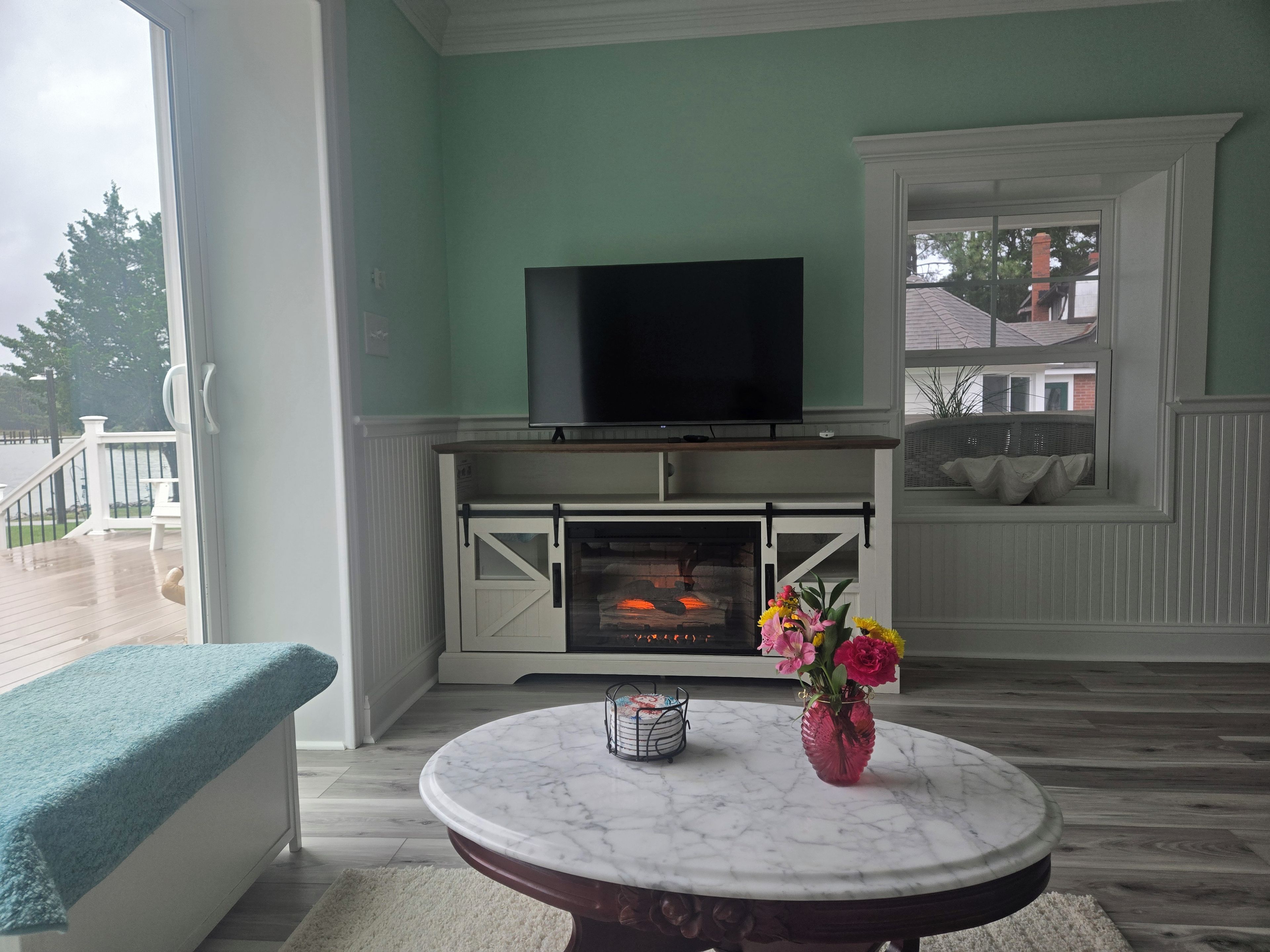 A living room with a fireplace, a television, and a round table with a vase of flowers.