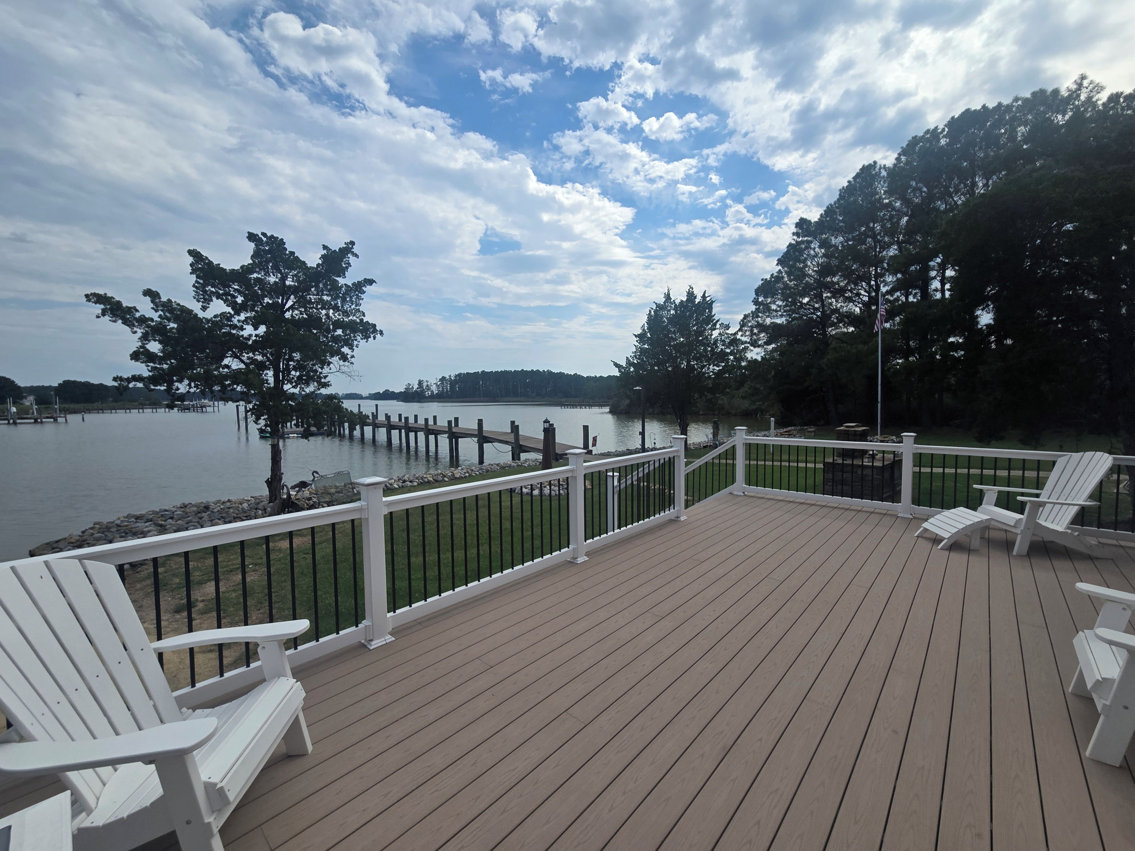 Una terraza de madera con barandillas blancas y sillas Adirondack con vista a un lago.