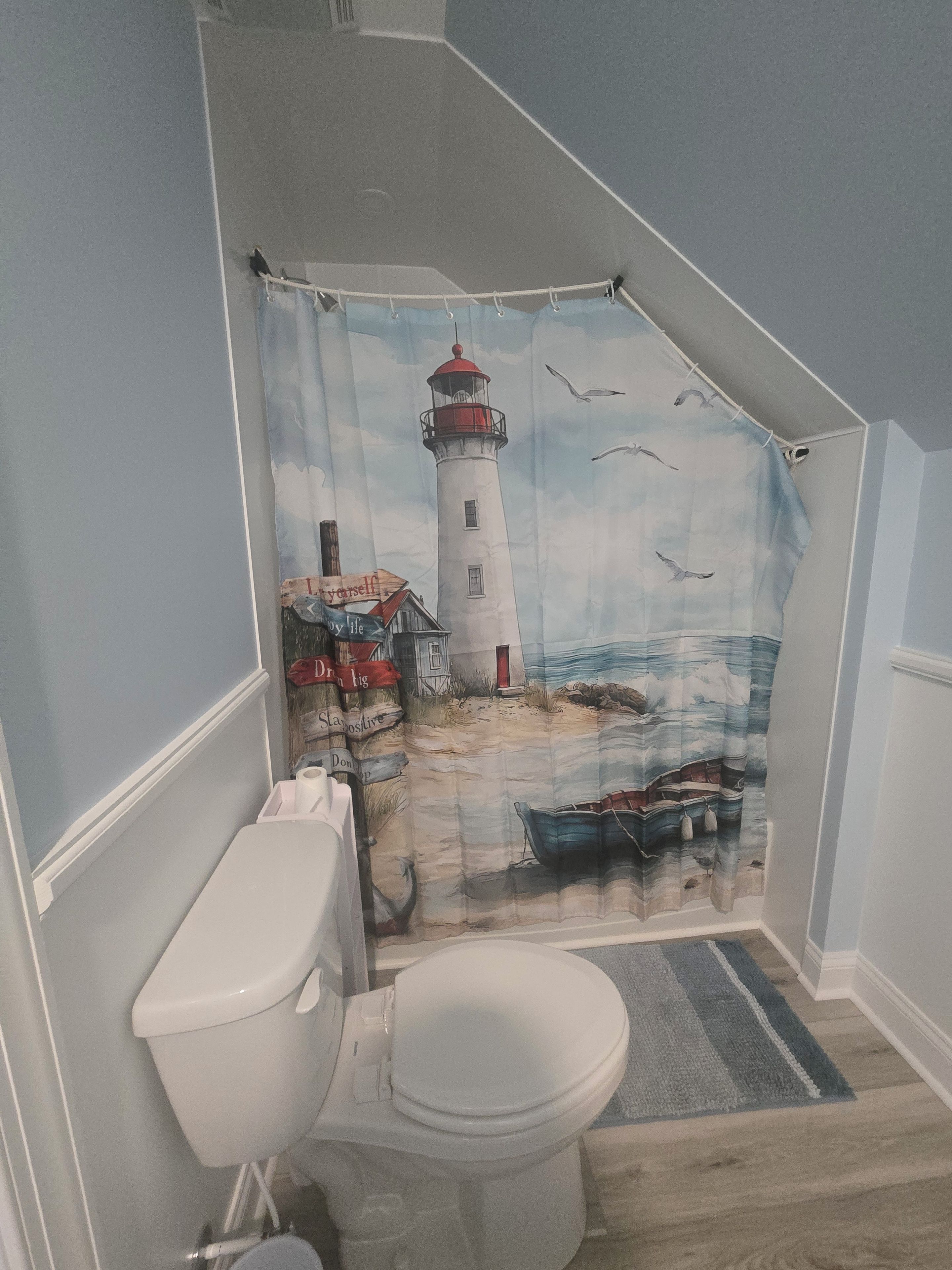 A bathroom with a nautical-themed shower curtain depicting a lighthouse, a toilet, and a small boat.