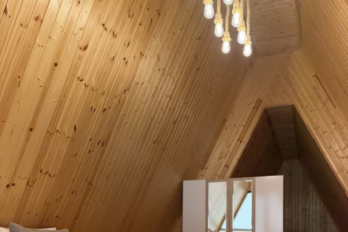 A high-ceilinged room with a sloped wooden ceiling, a bed with neatly folded white towels, and a patterned rug.