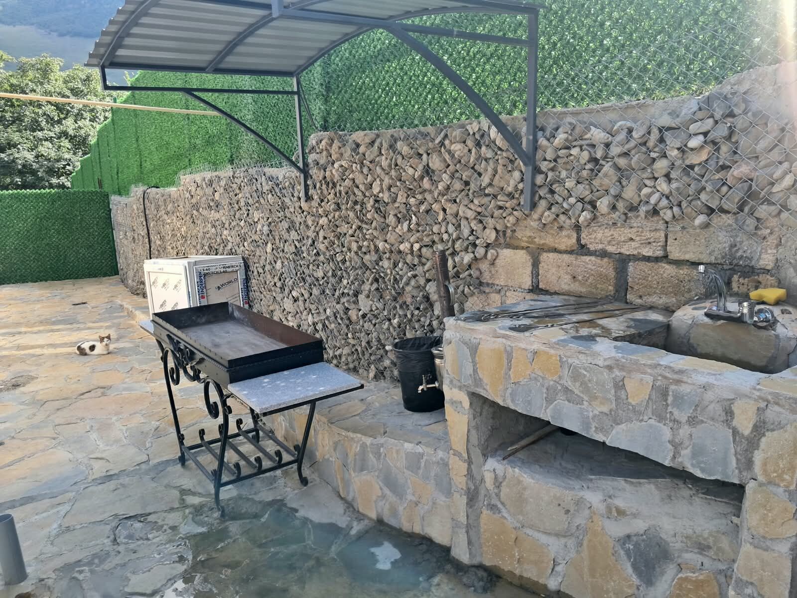 Et udendørs grillområde med stenvæg, grill og metalbord.
