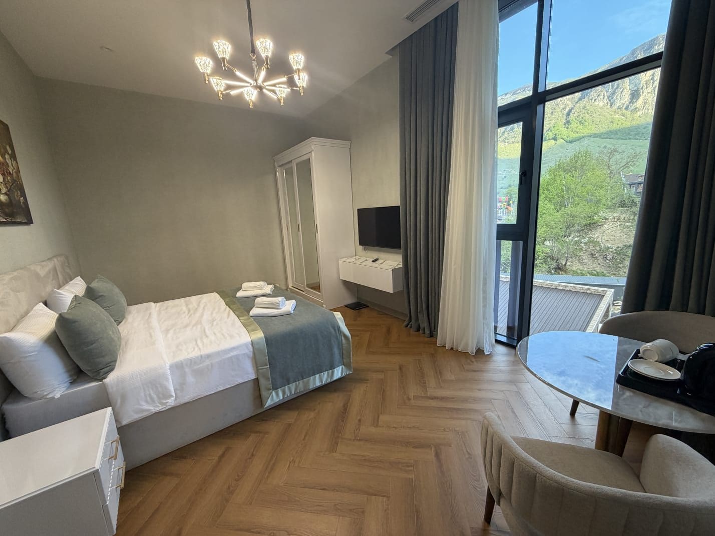 Habitación de hotel con cama, escritorio, silla, televisor y un ventanal con vistas al exterior.