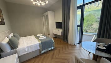 Habitación de hotel con cama, escritorio, silla, televisor y un ventanal con vistas al exterior.