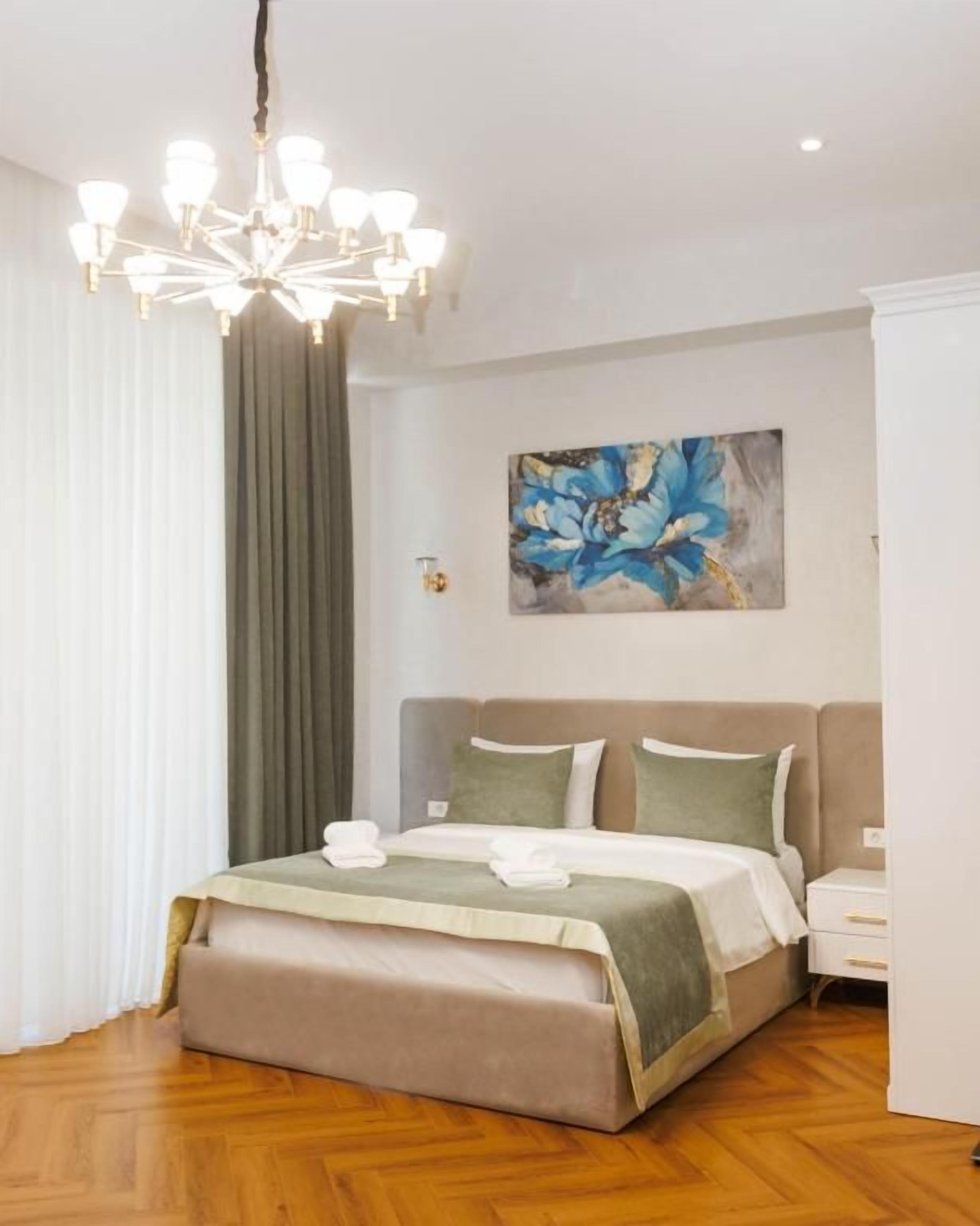 Una habitación de hotel con una cama, una araña, un cuadro y una mesita de noche.