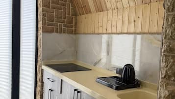 A kitchen with a stone wall, wooden ceiling, and a window with blinds.