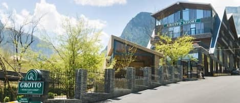A hotel entrance with a sign, a paved driveway, and a mountain backdrop.