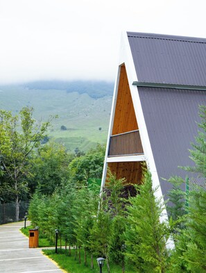 A modern building with a sloped roof, surrounded by lush greenery and a view of rolling hills.