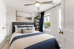 Ein Schlafzimmer mit einem Bett, einem Deckenventilator, einem Bücherregal und einem Fenster mit Vorhängen.