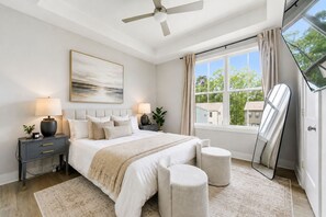 A bedroom with a bed, bedside tables, a ceiling fan, a window with curtains, and a large mirror. - Upscale Townhome 3 Ensuites Near BeltLine (Atlanta)