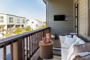 Een balkon met een rieten tafeltje, een witte bank en een televisie.