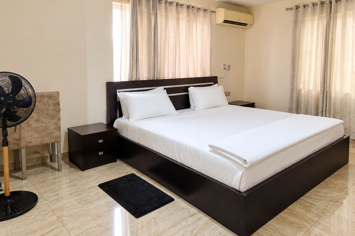 Ein modernes Hotelzimmer mit einem großen Bett, Nachttischen, einem Standventilator und einer Klimaanlage.