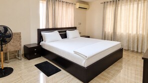 Ein modernes Hotelzimmer mit einem großen Bett, Nachttischen, einem Standventilator und einer Klimaanlage.