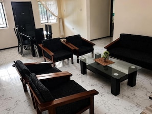 A living room with a sofa, two armchairs, a coffee table, and a dining table with chairs. - Princess Royal Lodge and Garden (Okpoma)