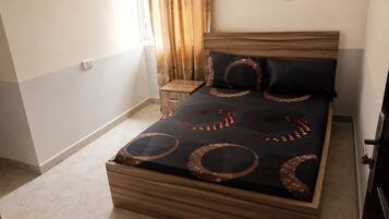 A bed with a patterned bedspread, a bedside table, and a window with curtains.