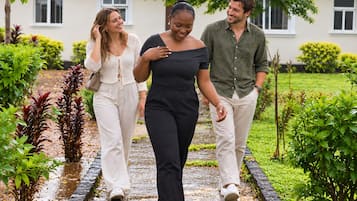 Three people walking on a wet pathway in a garden area with a building in the background.