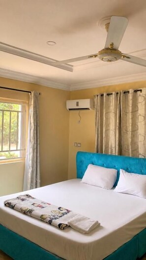 Ein Hotelzimmer mit Bett, Deckenventilator, Klimaanlage und einem Fenster mit Vorhängen.