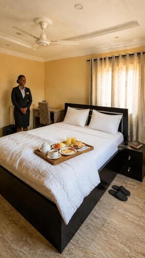 Ein Hotelzimmer mit Bett, Frühstücksbrettchen, Stehtisch, Koffer und Deckenventilator.
