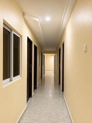 A hallway with doors on both sides, a tiled floor, and a light fixture on the ceiling. - Princess Royal Lodge and Garden (Okpoma)