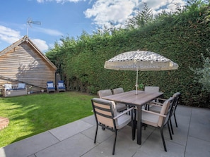 A patio with a table and chairs, a polka-dotted umbrella, and a wooden building with a sloped roof. - Foxley Lodge (Norwich)