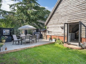 A patio with outdoor furniture and a covered area, a wooden building with a brick foundation, and a grassy yard. - Foxley Lodge (Norwich)