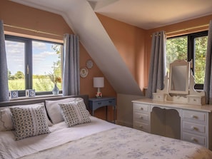 A bedroom with a bed, a dresser, a mirror, and a window with curtains. - Foxley Lodge (Norwich)