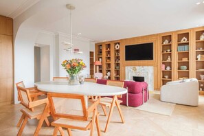 A modern living room with a round dining table, wooden chairs, a fireplace, and built-in shelving with decorative items. - Exceptional Duplex - Ac-4br/8p- Close to Marais (Paris)