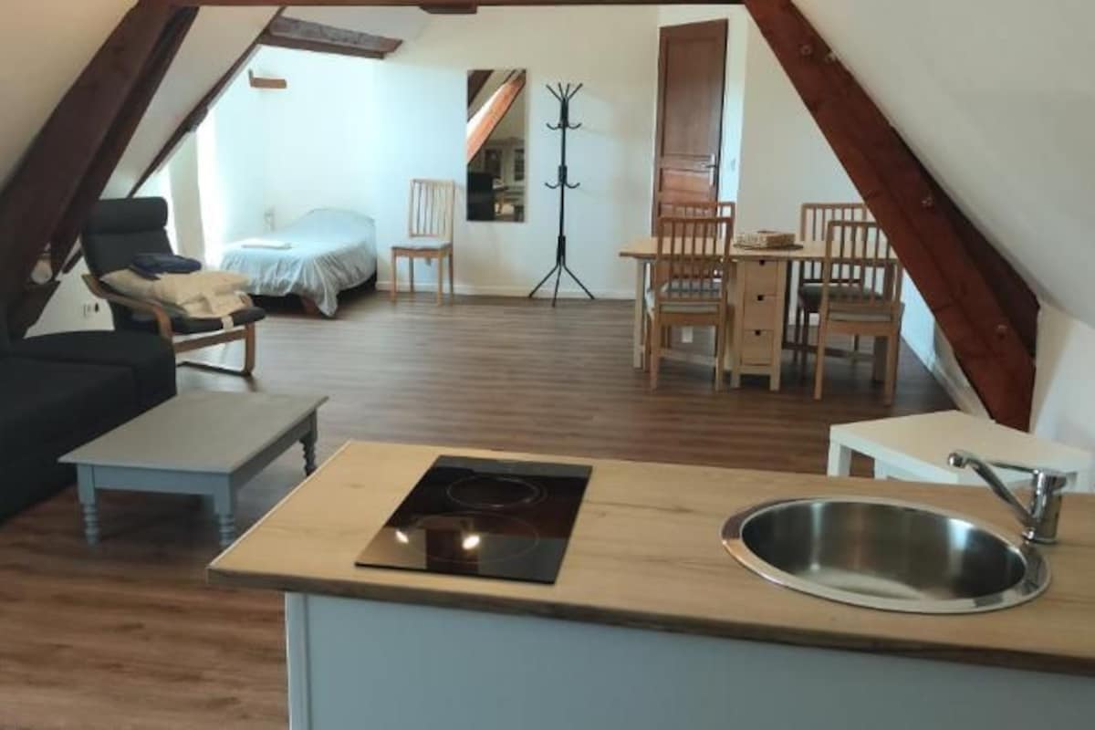 Et soveværelse på loftet med seng, stol, lille bord og trægulv.