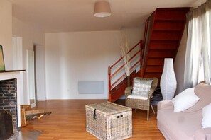 En stue med pejs, sofa, fletfodskanal, stol og trappe.