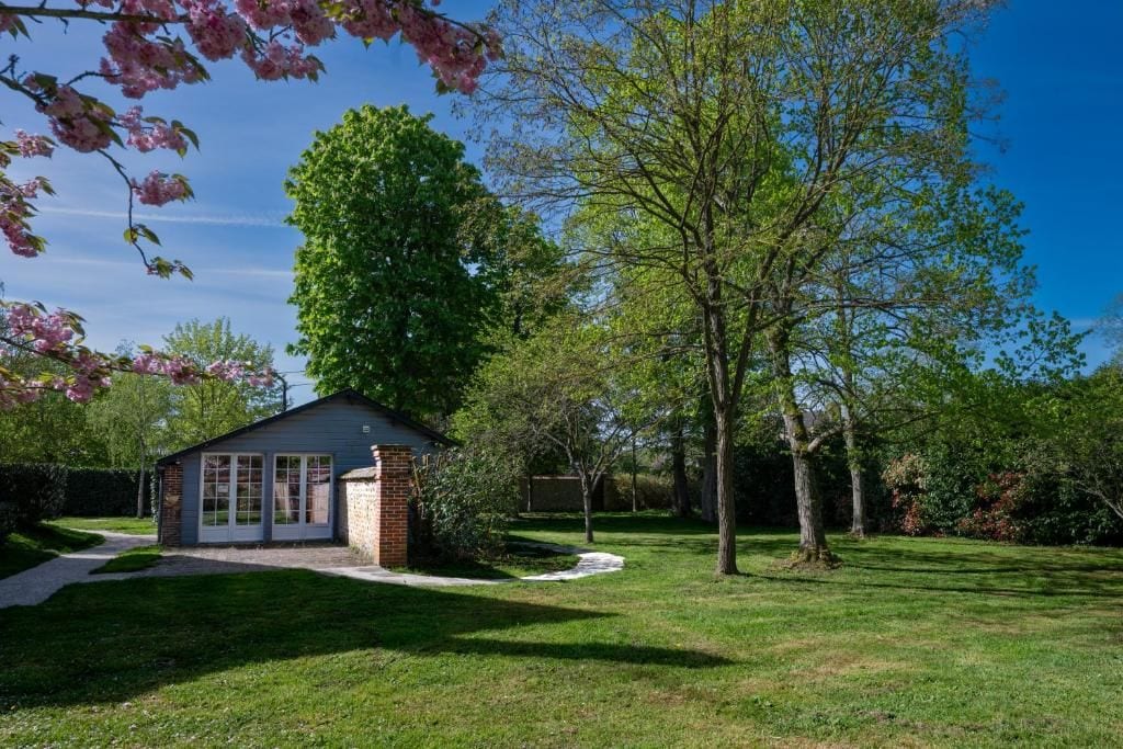 A single-story house with a brick chimney, a covered porch, and a lawn with trees.