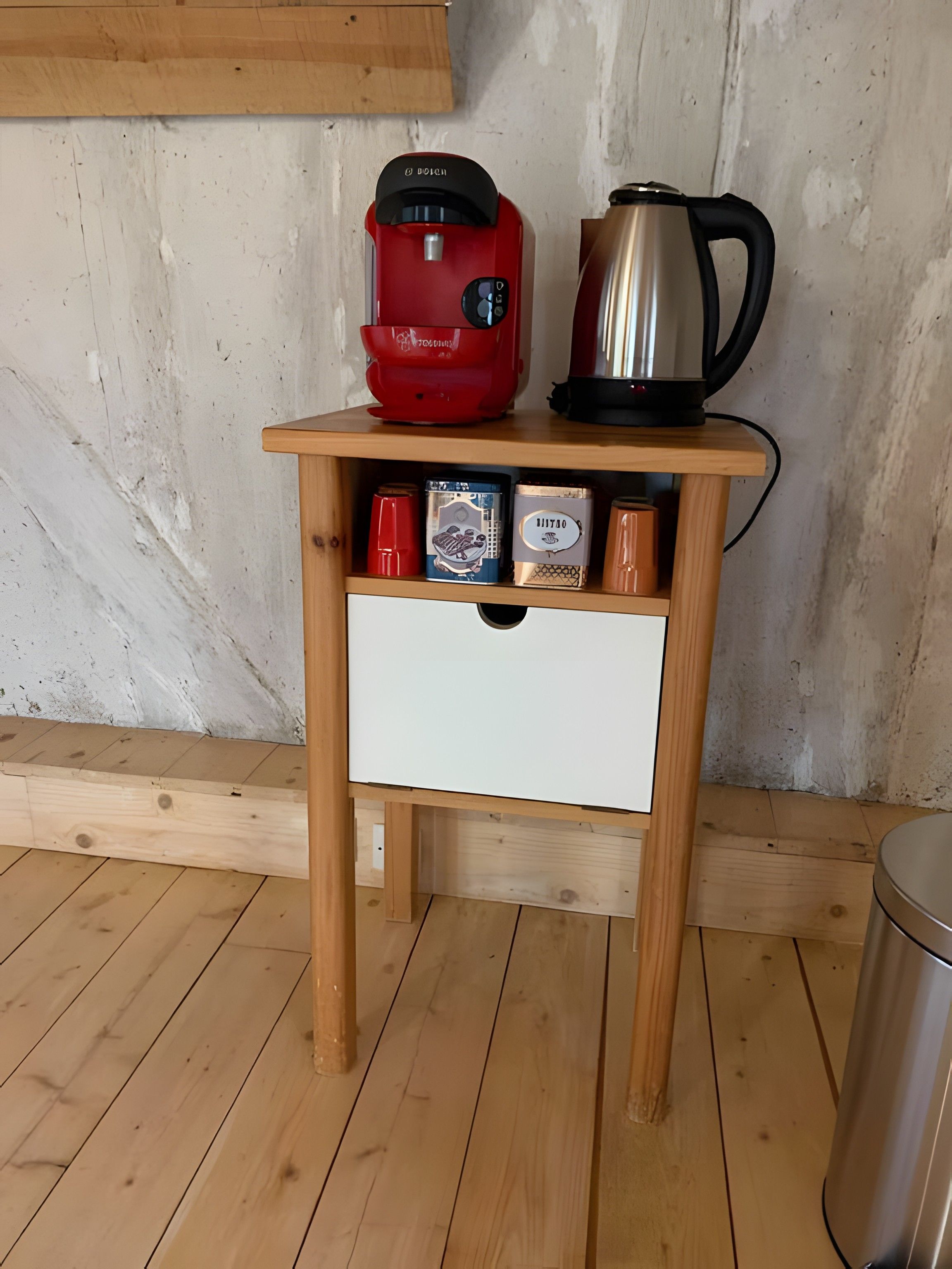 Una mesita de madera con una cafetera roja, un hervidor plateado y tres recipientes para especias.