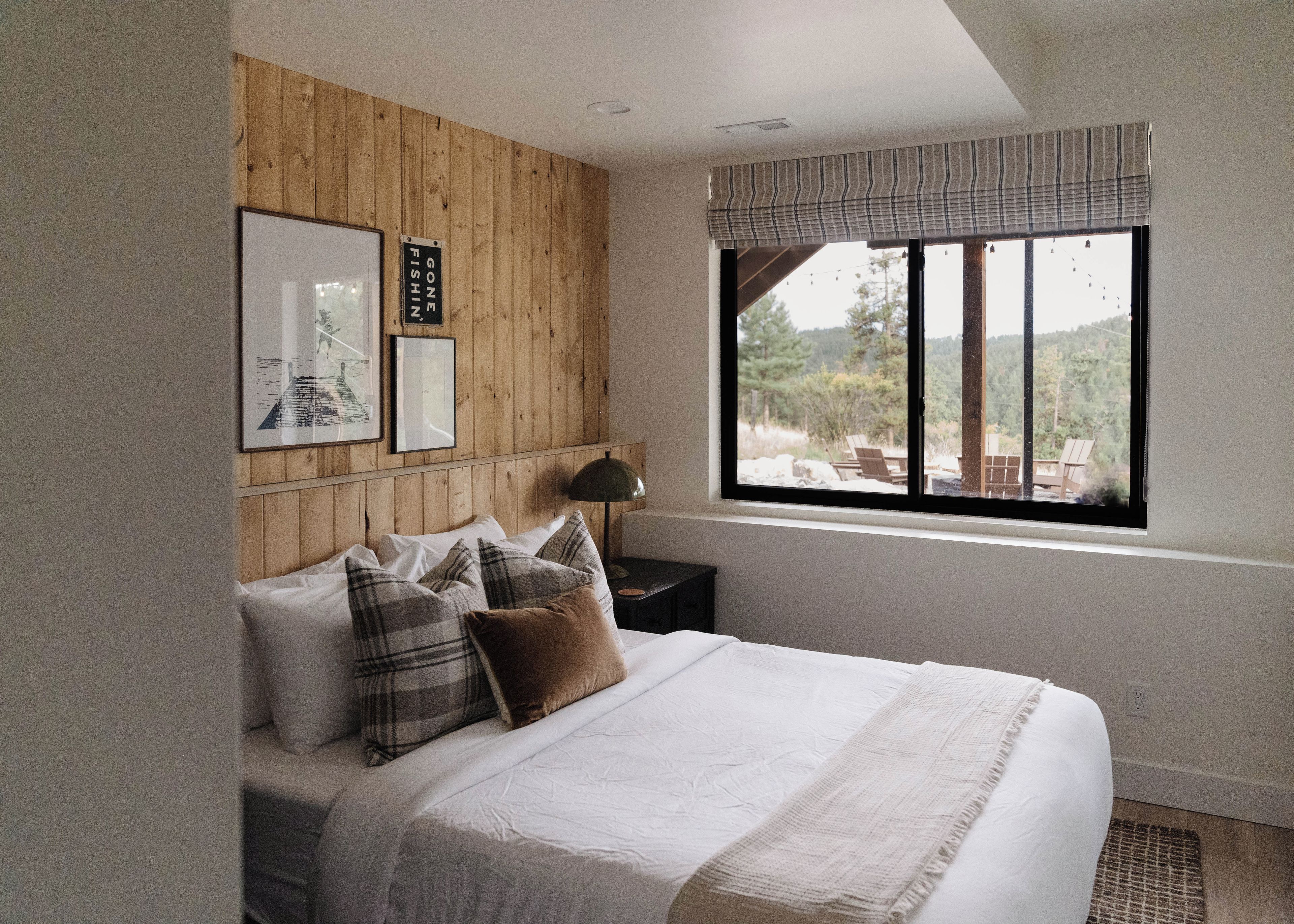 Une chambre à coucher avec une tête de lit en bois, un lit avec une literie blanche, une fenêtre donnant sur l’extérieur et une lampe fixée au mur.