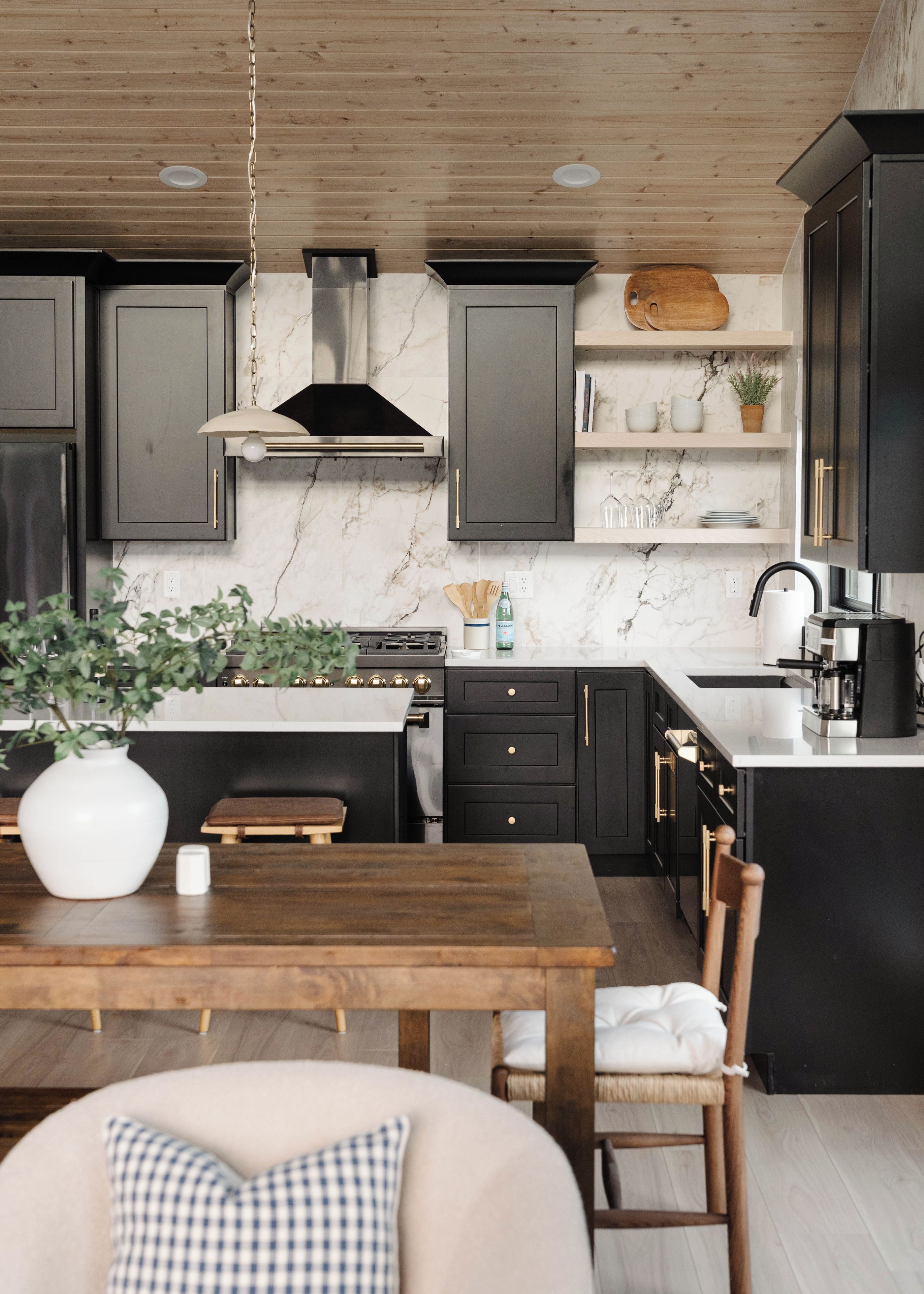 Une cuisine moderne avec des meubles de couleur sombre, un plan de travail en marbre et une table à manger en bois.