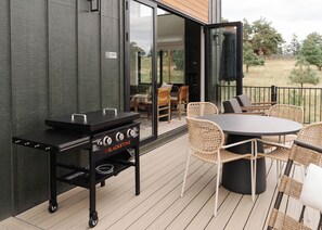 Eine Terrasse im Freien mit einem Blackstone-Grill, Korbmöbeln und Blick auf die umliegende Landschaft.