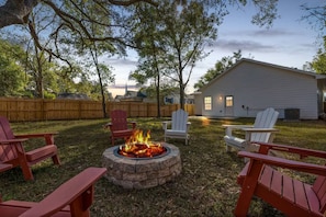 A backyard with a fire pit, outdoor seating, and a house.