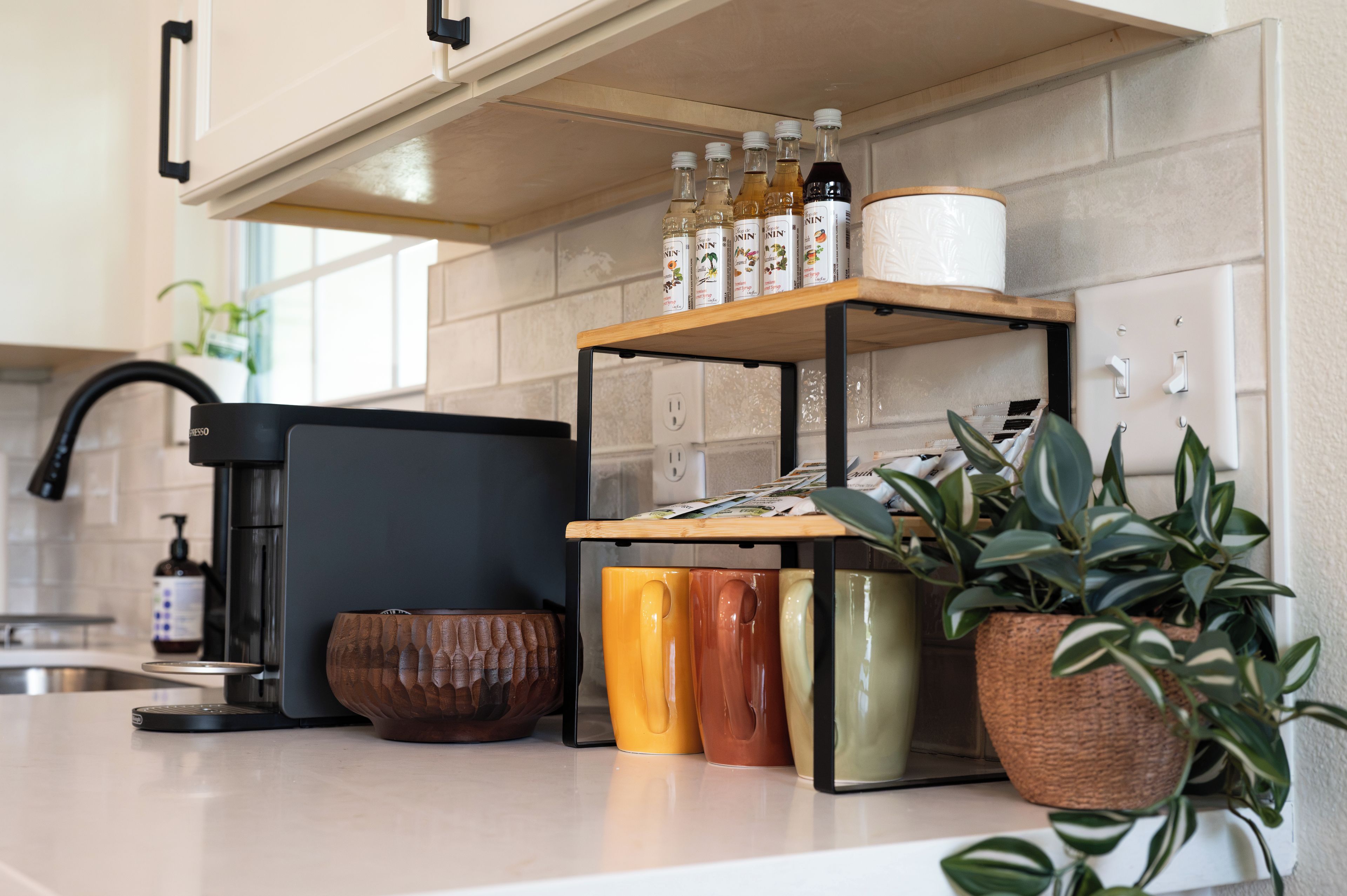 A kitchen with a coffee machine, a shelf with bottles, and a potted plant.