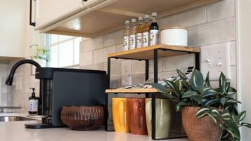 A kitchen with a coffee machine, a shelf with bottles, and a potted plant.