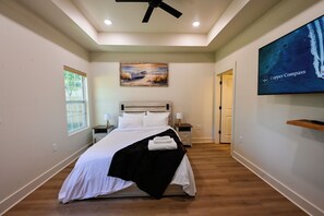 Un dormitorio con cama, mesita de noche, un cuadro, televisor y una puerta.