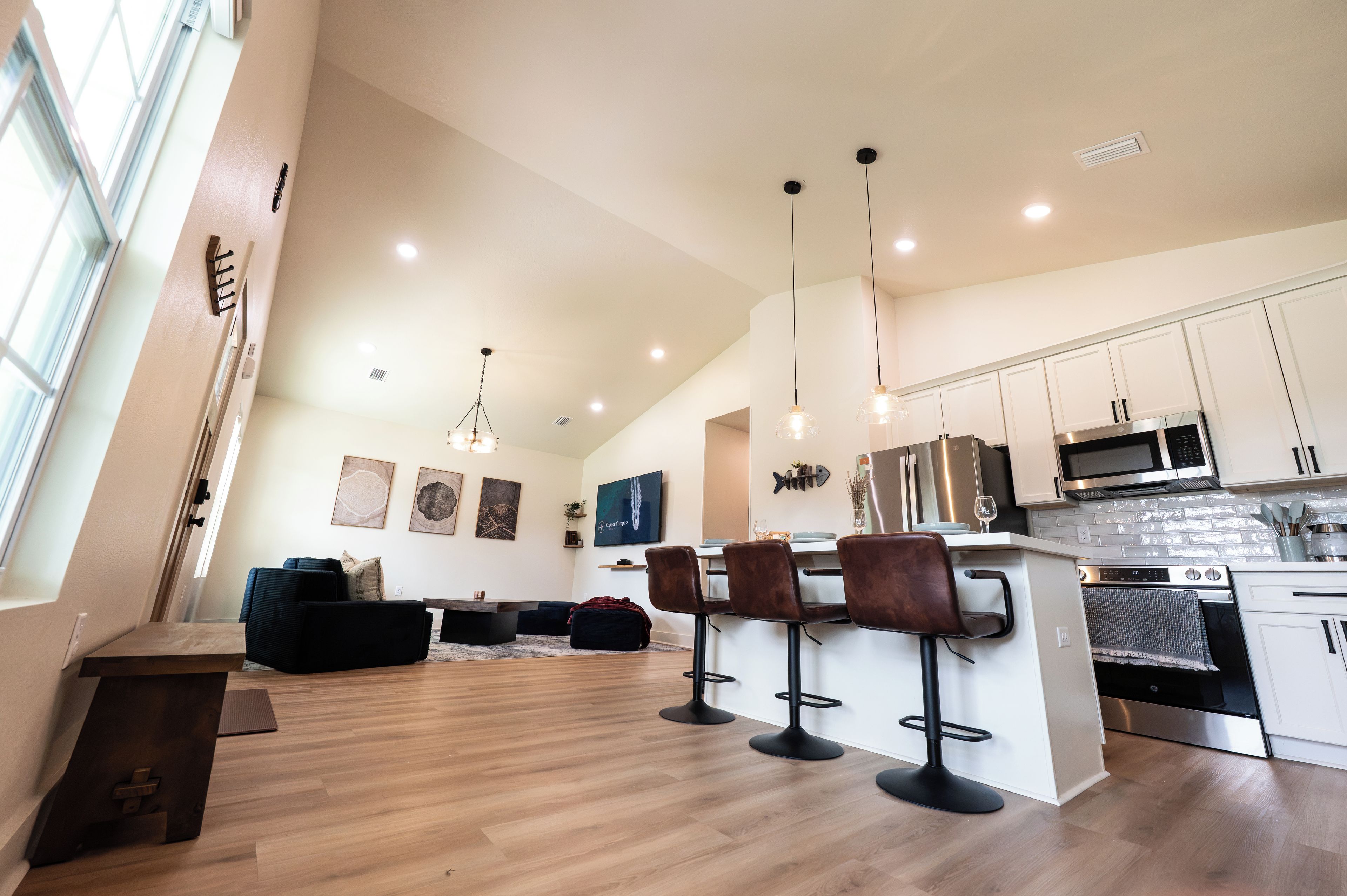 A modern kitchen with bar stools, a dining area with a sofa, and artwork on the walls.