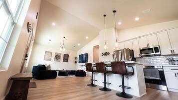A modern kitchen with bar stools, a dining area with a sofa, and artwork on the walls.