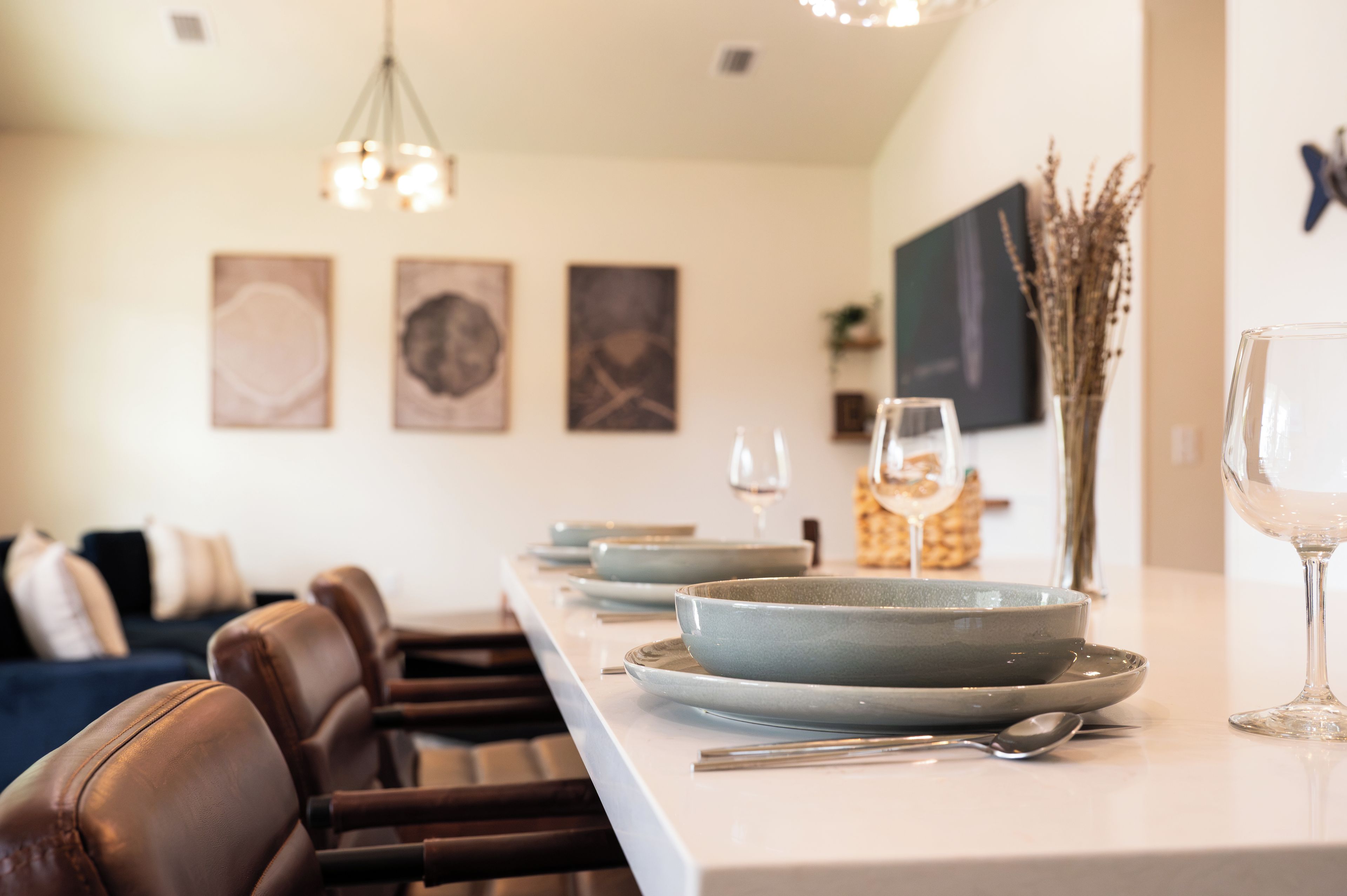 A dining area with a long table set for two, a vase with dried plants, and a television mounted on the wall.