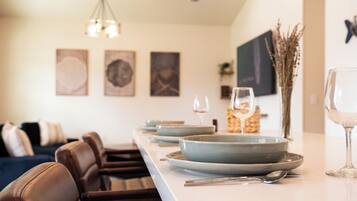 A dining area with a long table set for two, a vase with dried plants, and a television mounted on the wall.
