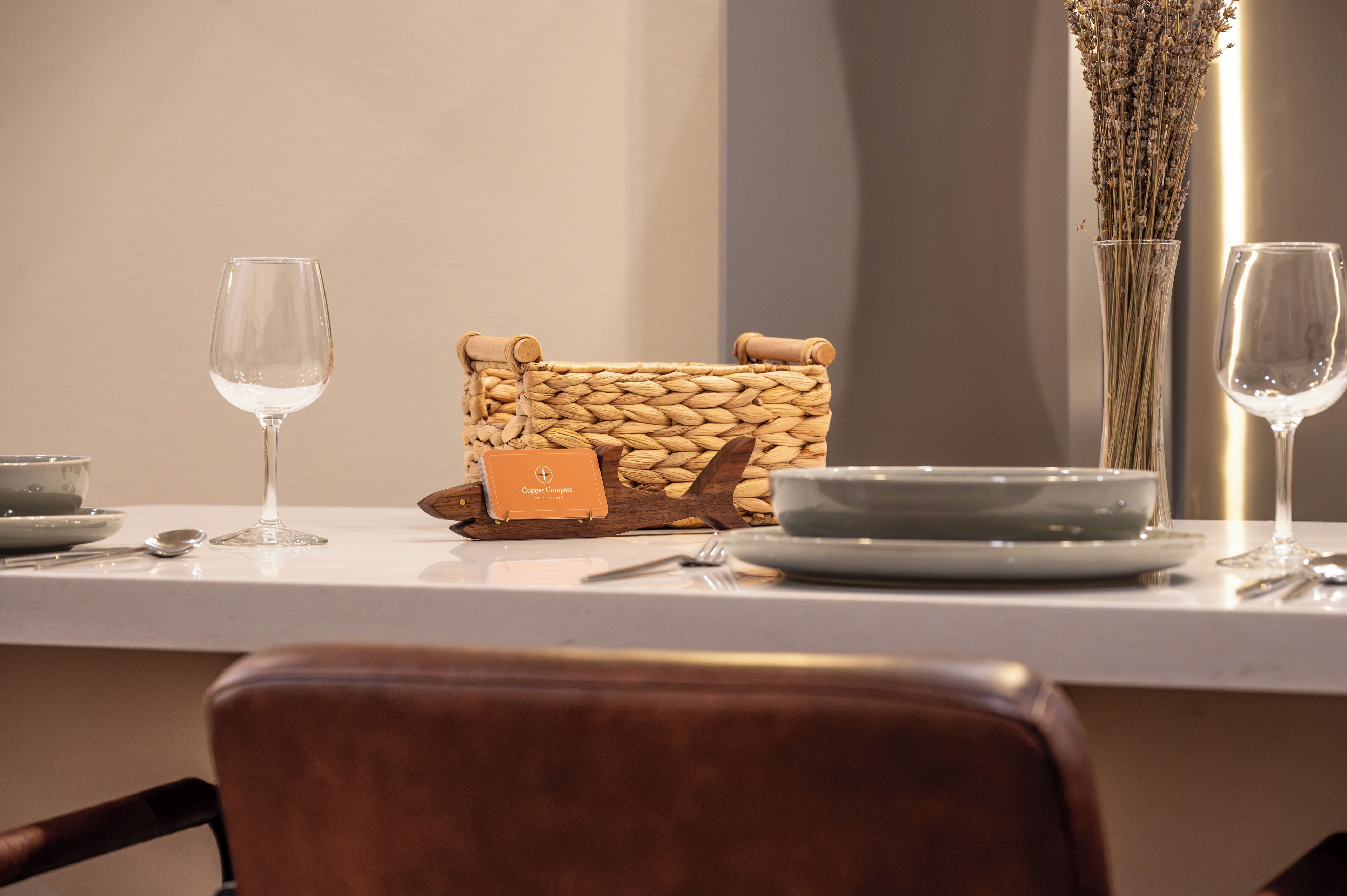 Une table à manger est dressée avec des assiettes, des couverts et deux verres à vin. Un sac en tissu, muni d’une étiquette, est posé sur la table.