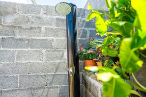 A showerhead attached to a brick wall, with potted plants nearby. - Hostcare - Studio Piton - Swimming pool & Hiking (Saint-Louis)