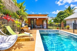 A swimming pool with a wooden deck, lounge chairs, and a small garden area with tropical plants. - Hostcare - Studio Piton - Swimming pool & Hiking (Saint-Louis)