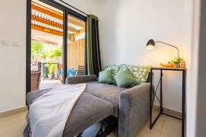 A room with a bed, a table with a lamp, and a view of the outdoors. - Hostcare - Studio Piton - Swimming pool & Hiking (Saint-Louis)